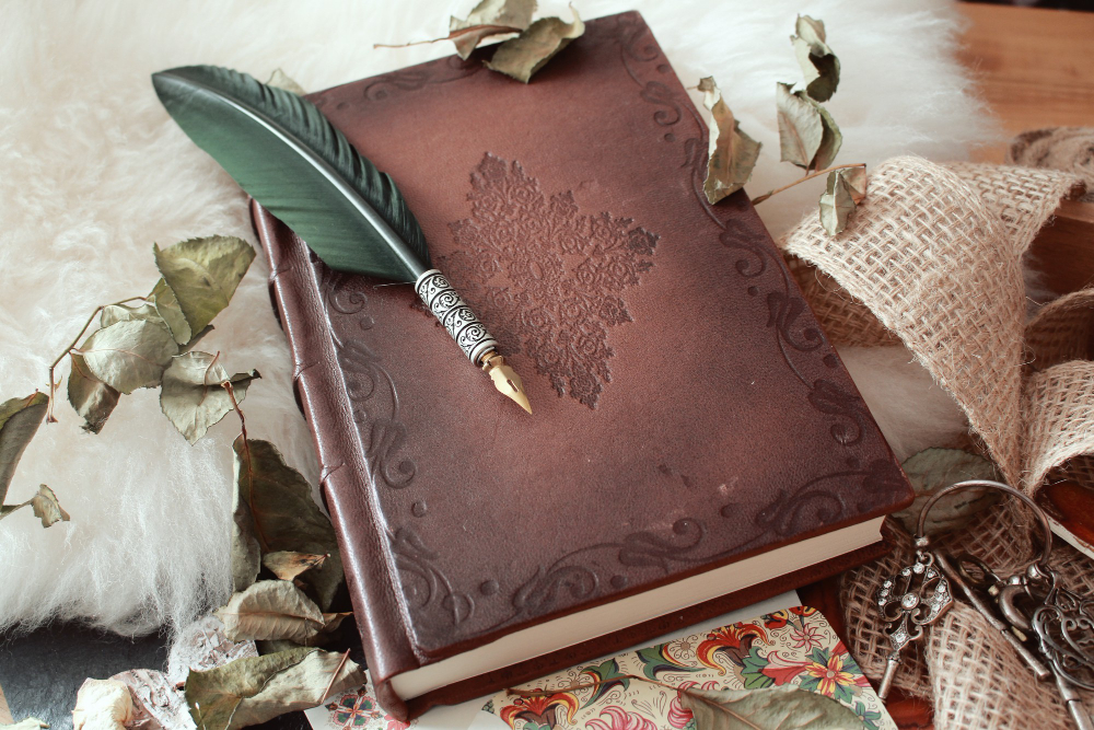 High angle shot of a quill pen and an old book covered with dried flower petals